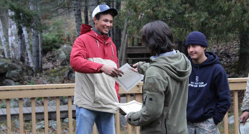 Three people speak and exchange papers during the family seminar of an outward bound intercept course.